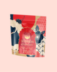 The "London Fog Rooibos" tea package is vibrant with cranes, stylized waves, and floral patterns in red, blue, and gold. It features rooibos and highlights "Caffeine-Free" and "Made with Love.