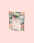 A pastel pink package of "London Fog White" tea features vibrant peacocks and tropical flowers in teal and coral, with a hint of bergamot. The design is elegant and lively, creating an exotic and luxurious feel.