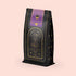 The "Lucid Dreams" Herbal Tea Refill Pouch is a black, gold, and purple bag of Magic Hour turmeric tulsi tea with an elegant hourglass and celestial design. The label reads "Lucid Dreams" and "Time for Infinity." This caffeine-free blend stands against a light beige background.
