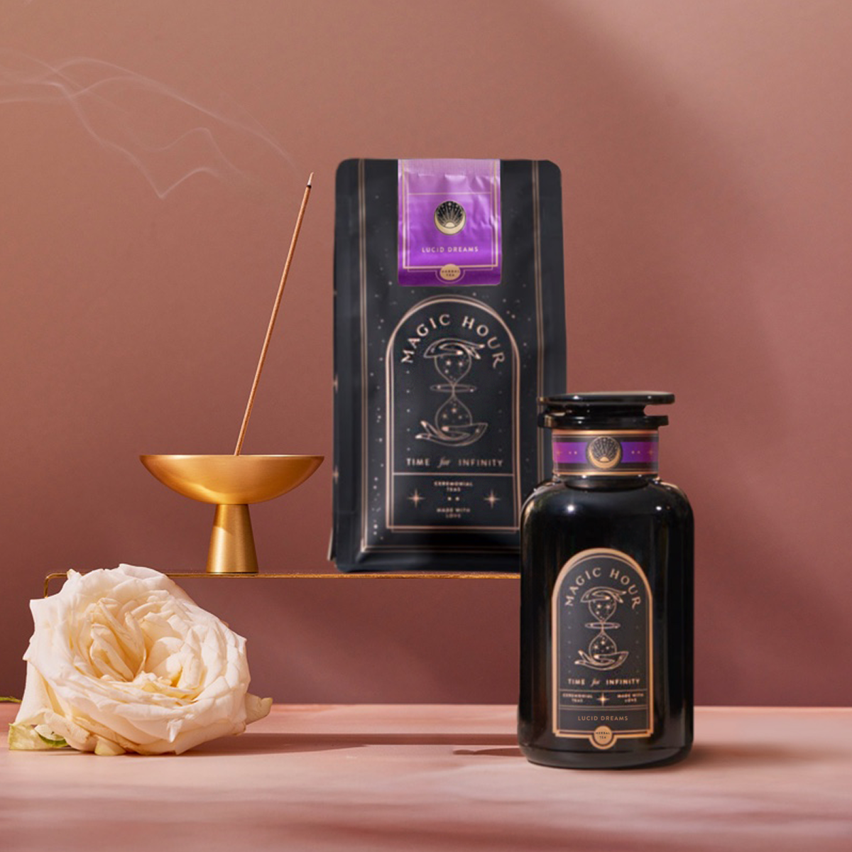 The Lucid Dreams Starter Kit: Tulsi-Turmeric Herbal Tea for Sleep & Calm is shown on a pink surface with a white rose and incense burner—ideal for your nighttime tea or soothing tulsi chai ritual.