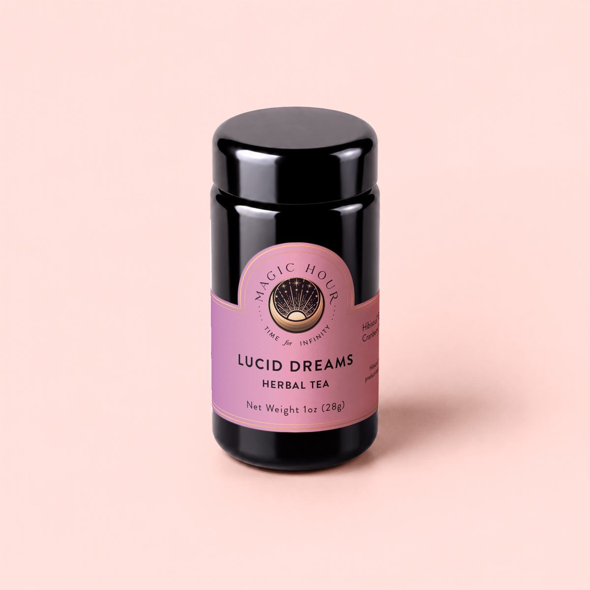 A black jar of Magic Hour Lucid Dreams: Tulsi-Turmeric Herbal Tea for Sleep &amp; Calm with a purple label sits on a light pink background. The label displays the product name, weight (1oz/28g), and decorative gold accents, highlighting this soothing, caffeine-free chai infused with restful botanicals to support sleep and calm.
