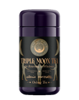 A purple cylindrical container labeled "Triple Moon Tea by Alanis Morissette to Celebrate her Triple Moon Tour!" with gold accents. The label features text "for Returning to Wholeness," "Ceremonial teas," "Made with love," and "Magnolia Oolong Tea" along with crescent moon designs and a central logo reading "Magic Hour.