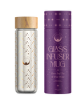 A double-walled borosilicate glass infuser mug with a wooden lid adorned with a celestial design of stars and moons sits next to its matching purple cylindrical packaging. The packaging, labeled Glass Infuser Mug for Loose Leaf Tea & Fruit Water," features a starry pattern that complements the mug's design.