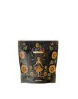 A black packaging bag with floral designs, featuring a central tarot card illustration labeled "The Sun." The design includes a crowned figure surrounded by sunflowers and celestial motifs. Notably, this Magic Hour blend, named "The Sun: Energizing Adaptogenic Herbal Tea with Yaupon, Moringa & Turmeric," contains rejuvenating ingredients like Moringa and Turmeric Root.