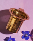 Product Name: Loose Leaf Tea Starter Set

A gold metal tea infuser from the Loose Leaf Tea Starter Set, featuring an intricate mesh design, rests on a pink surface and casts a shadow. Nearby, two blue flowers enhance the scene with their vibrant color.