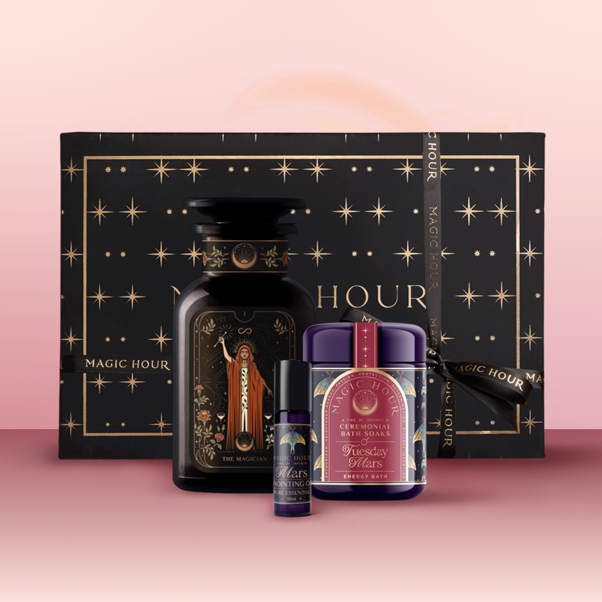 The Mars Bath & Beauty Box features a black and gold star-patterned box, dark apothecary jar, small perfume vial, and purple tea canister, artfully arranged as part of a ritual collection on a soft pink gradient background.