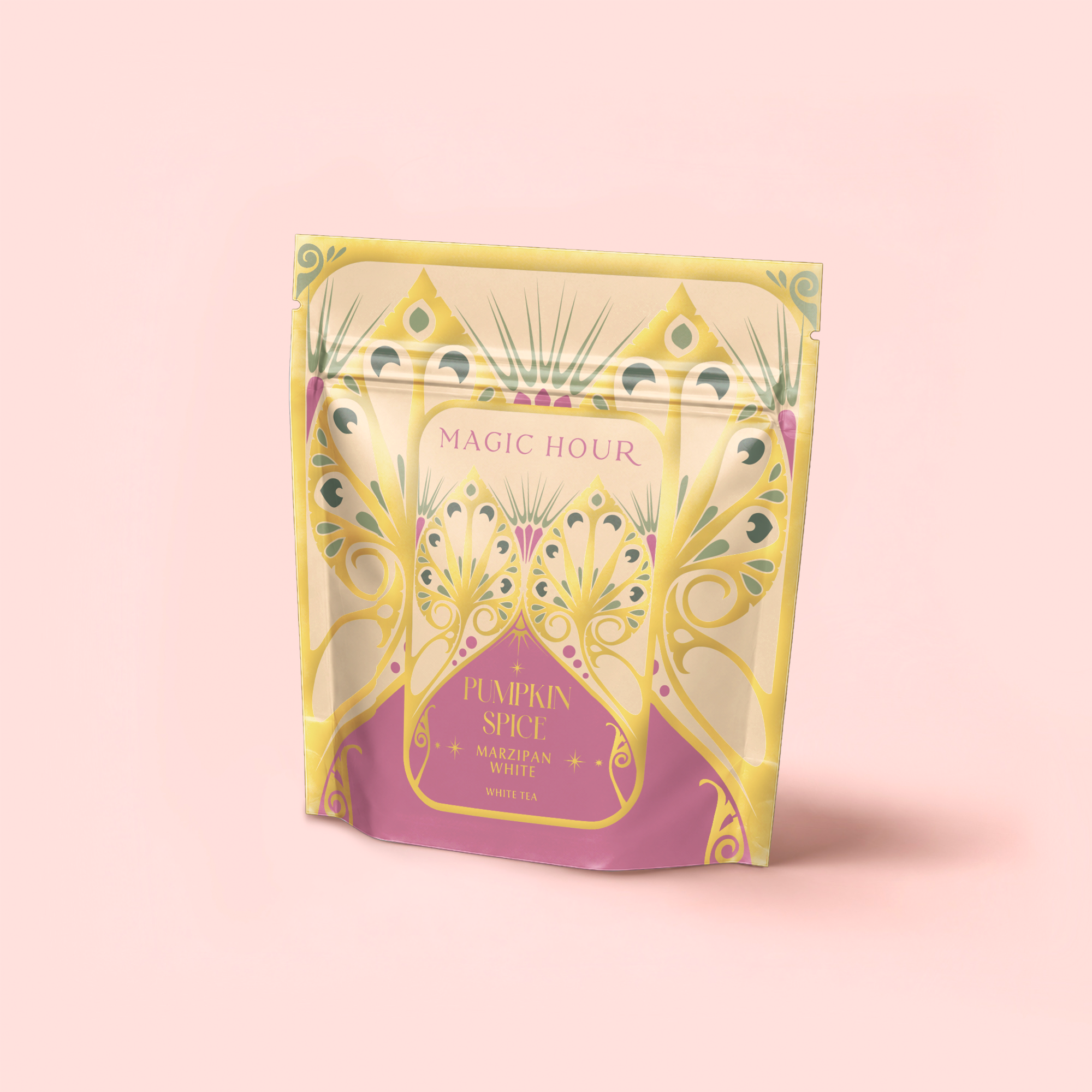 A pastel tea package labeled "Magic Hour" stands upright, featuring gold, green, and purple Art Deco designs. The label reads "Pumpkin Spice Marzipan White Tea." Set against a soft pink background, it has a decorative flair.