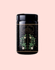 A black jar labeled "Matcha Herbed Salt" features gold text, green leaf and white flower illustrations, and decorative stars, all set against a pale pink background.