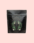 A resealable black pouch labeled "Matcha Herbed Salt," featuring gold stars and botanical designs, sits on a light pink background. The packaging displays "Seasonings" and "Culinary Tea Seasoning.
