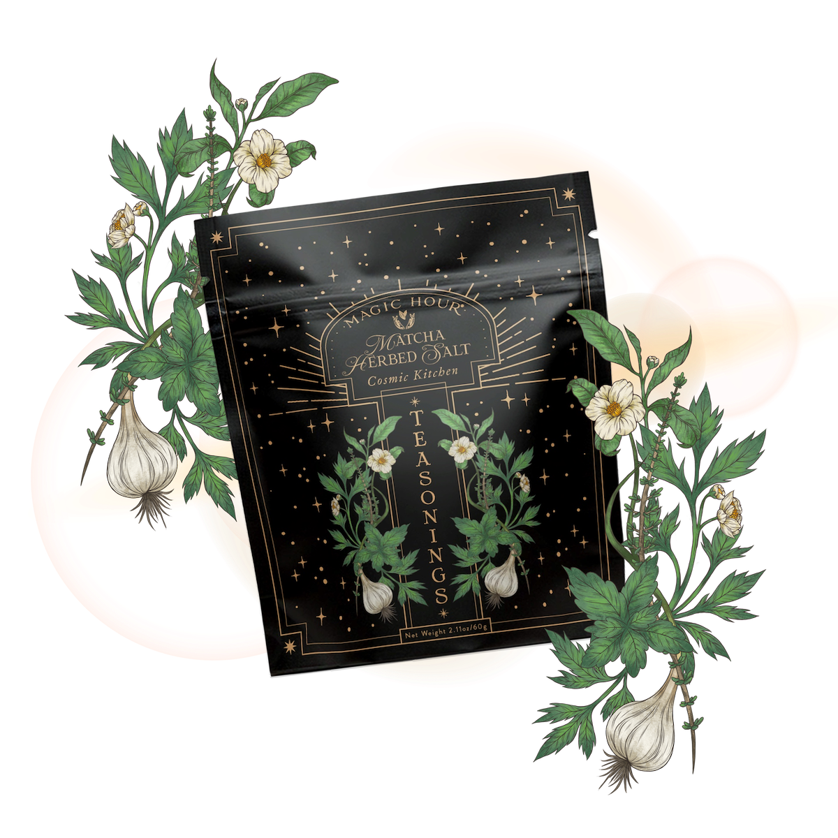A black packet of Matcha Herbed Salt, adorned with golden stars and botanical designs, is displayed among green leaves, white flowers, and garlic bulbs—a vibrant showcase of this gourmet seasoning blend on a light background.