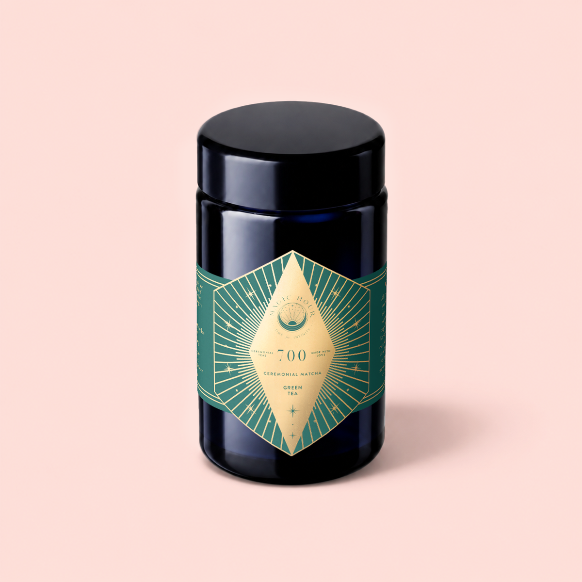 A dark jar featuring a gold and green geometric label with “Organic Ceremonial Matcha 700” sits on a light pink background, emphasizing the premium quality of this organic ceremonial matcha sourced from Kagoshima.