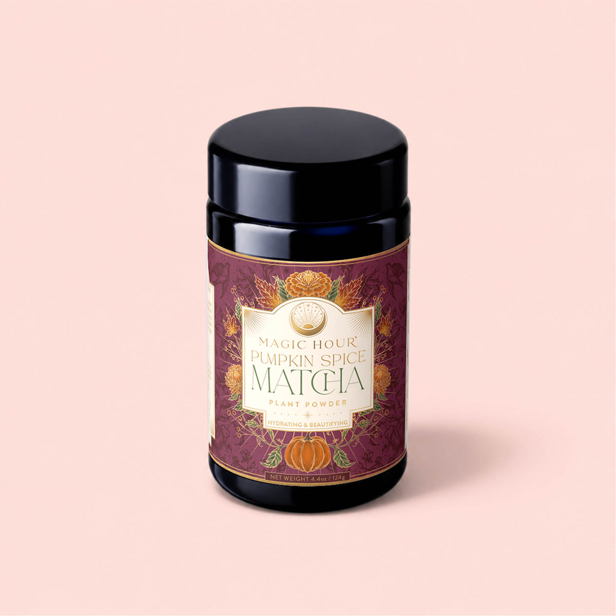 A black jar labeled “Pumpkin Spice Matcha” with festive orange pumpkins and foliage—evoking autumn botanicals—adorns a dark maroon and gold label, displayed against a pale pink background. This seasonal blend features matcha infused with pumpkin spice for a unique autumn twist.