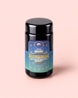 A dark jar with a colorful label reading “Mercury Mint Nighttime: Vanilla Mint Lavender Jasmine Tea – Caffeine Free!” sits on a light pink background. The label, adorned with celestial designs and text in gold, blue, and teal hues, hints at this herbal tea’s calming blend of vanilla, mint, lavender, and jasmine—specially crafted for gentle digestion support without caffeine.