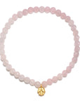 The Rose Quartz Mini Hamsa Bracelet features translucent pink Rose Quartz beads arranged in a circular pattern, highlighted by a small golden Hamsa hand charm that prominently hangs at the bottom center. The background is plain white.