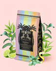 A pastel-striped coffee bag labeled "Mojito Mint: Green Mint Mocktail Tea for Bright Moods & Celebrating Clarity" stands surrounded by mint leaves, lime slices, and a yellow snake on a light pink background, evoking the fresh flavors of a zero-proof cocktail or an invigorating Mojito Mint Green Tea.