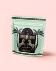 A mint-green resealable pouch labeled "Mojito Mint: Green Mint Mocktail Tea for Bright Moods & Celebrating Clarity" with two zebras and palm trees stands against a pale pink background, perfect for refreshing zero-proof cocktails.