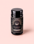 A black jar labeled “Mood Balance: Breakfast with Benefits” rests on a light pink background. The label is adorned with gold sunburst designs and celestial motifs, evoking the calming qualities of herbal breakfast tea blends like lion’s mane and ashwagandha. The jar displays a net weight of 3oz/84g.