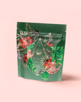 A packaging pouch for Moonlight in Marrakesh: Spiced Mint Green Tea features tropical floral and leaf illustrations, monkeys, and a teapot on a light pink background. The label reads "Moonlight in Marrakesh: Spiced Mint Green Tea.