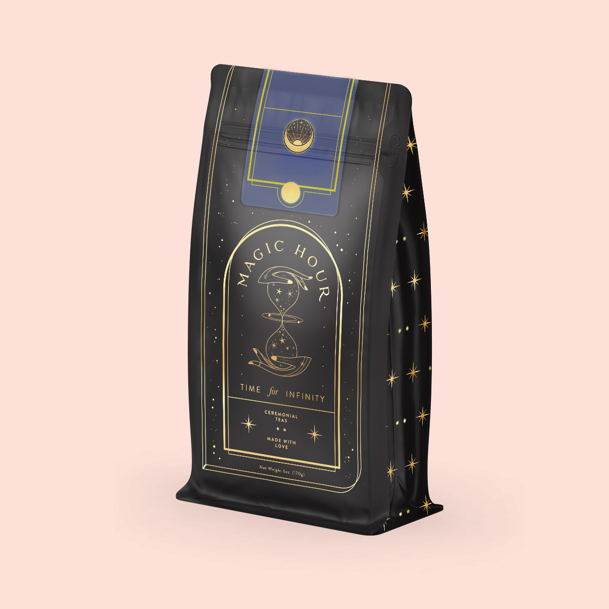 A standing dark bag with gold and blue accents displays the "Magic Hour" label, featuring an hourglass illustration. Star-like details hint at Moringa Moon Herbal Tea's digestive benefits. It rests on a light pink background.