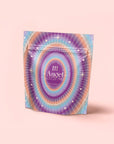 A vibrant, iridescent pouch labeled "111: Lavender-Jasmine-Pineapple Herbal Tea with Blue Lotus" rests on a pastel pink background. The packaging features gradient purple, blue, and gold concentric circles and stars for crown chakra activation.
