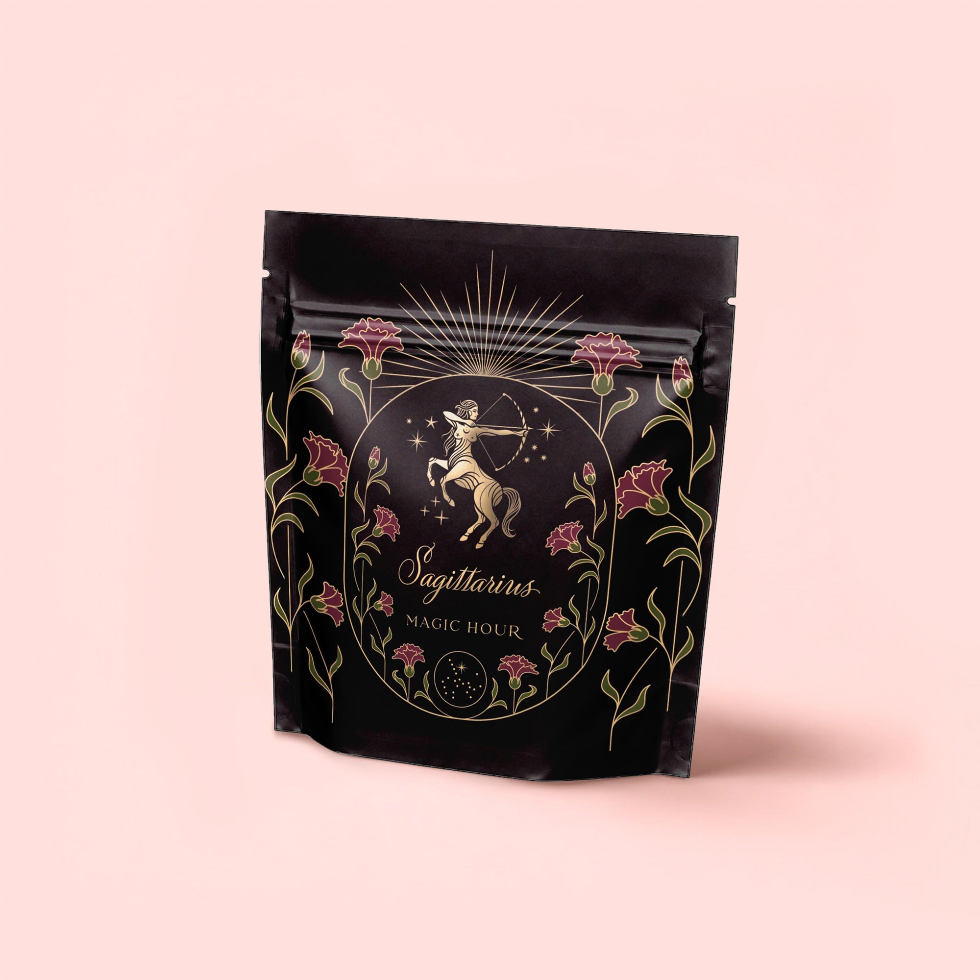 A black pouch with gold and pink centaur archer designs, labeled "Sagittarius Tea of Good Fortune &amp; Abundance," features stars and florals and highlights its pomegranate ginger blend, set against a pale pink background.