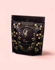 A black resealable pouch with gold floral designs and a celestial figure holding stars. The soft pink label reads “Virgo” and “Magic Hour,” featuring the Virgo Tea of Virtue, Wit & Meticulous Magic organic black tea blend.