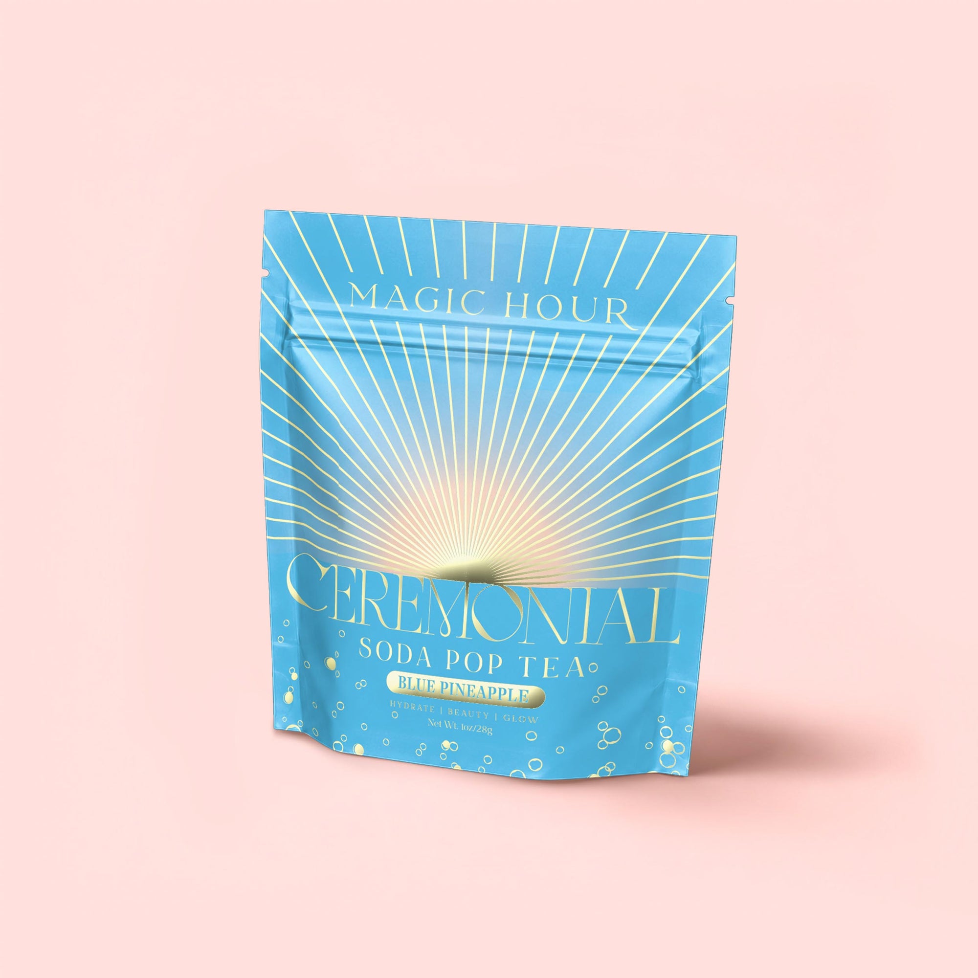 A blue and gold stand-up pouch labeled "Blue Pineapple: Ceremonial Soda Pop Tea" sits against a pink background, adorned with sunburst graphics and bubbles—made with blue spirulina and caffeine-free herbal tea.