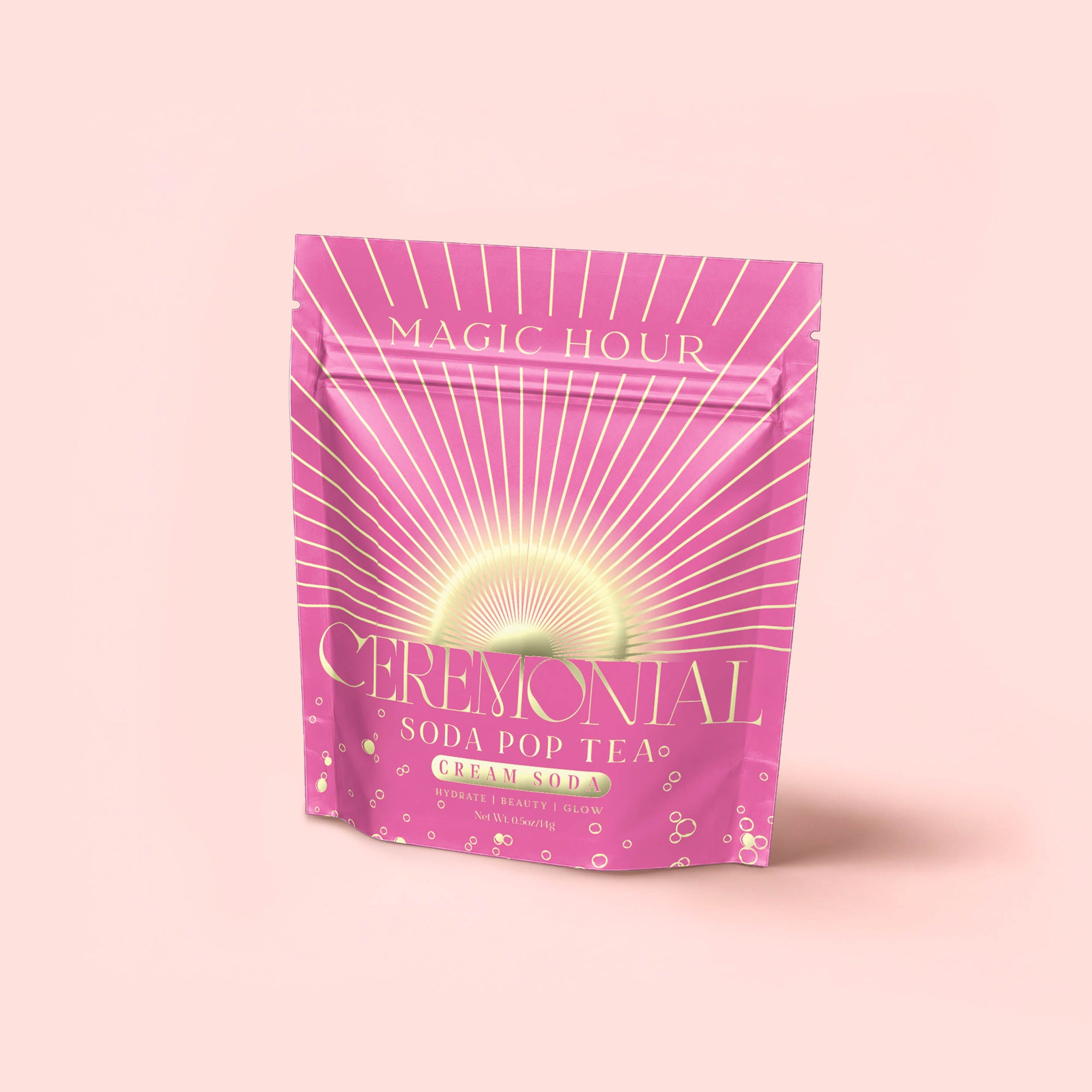 A pink resealable pouch labeled "Cream Soda White Tea: Ceremonial Soda Tea" with golden rays and bubbles stands upright against a light pink background—this blend is a delightful cream soda-inspired white tea.