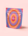 A vibrant, holographic pouch with radiant lines and stars on pink reads "777: Celestial Messengers Dawn Pineapple Passionfruit Green Tea," blending tropical flavors for a spiritually uplifting experience.