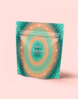 A teal and orange resealable pouch labeled "888: Lemon-Jasmine-Vanilla Herbal Tea" features radiating white lines and small stars, standing upright on a pale pink background.