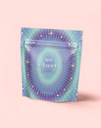 A pastel pink, iridescent resealable pouch labeled "999: Adaptogenic Pineapple-Mint-Jasmine Herbal Tea" features starburst and star designs, offering herbal support for peaceful sleep and spiritual completion.
