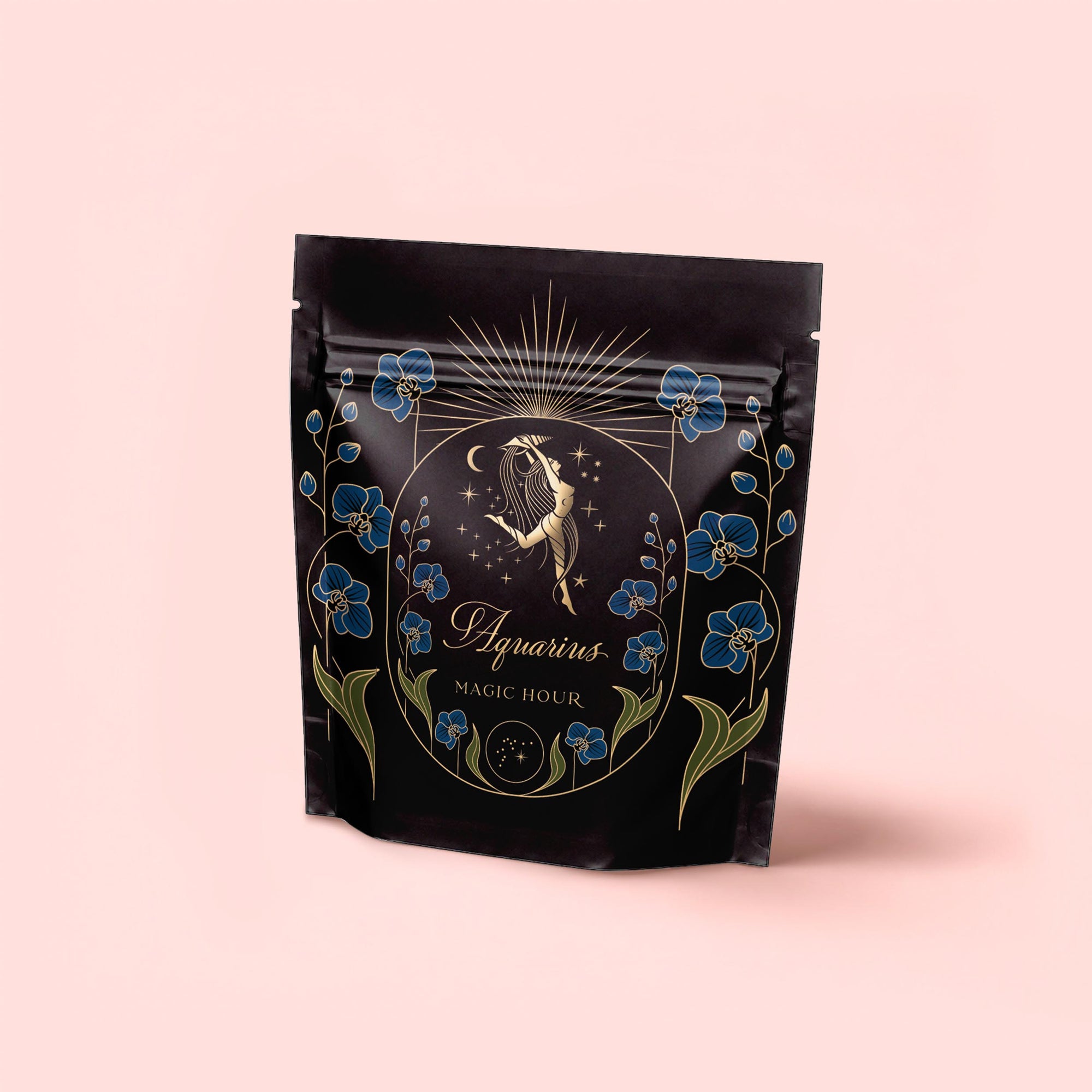 A black pouch with gold and blue floral designs features a woman pouring water, stars, and "Aquarius: Visionary Goddess Tea," hinting at the vanilla-infused black tea inside, set on a pale pink background.