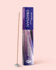 A box of Natural Incense : Obsidian labeled “Hope” stands upright beside a lit incense stick releasing calming sandalwood notes from a small round holder—all set against a pale pink background.