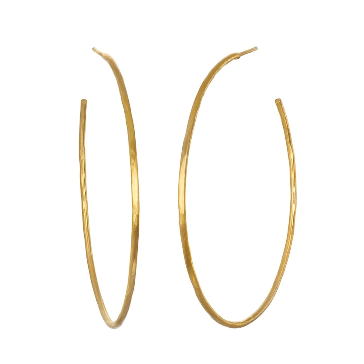 A pair of large, thin, gold hoop earrings with a simple, elegant design. The Ongoing Energy Large Hoop Earrings by Magic Hour are slightly oval-shaped and have a smooth, polished finish that gleams like hammered 18KT gold plate.