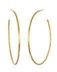 A pair of large, thin, gold hoop earrings with a simple, elegant design. The Ongoing Energy Large Hoop Earrings by Magic Hour are slightly oval-shaped and have a smooth, polished finish that gleams like hammered 18KT gold plate.