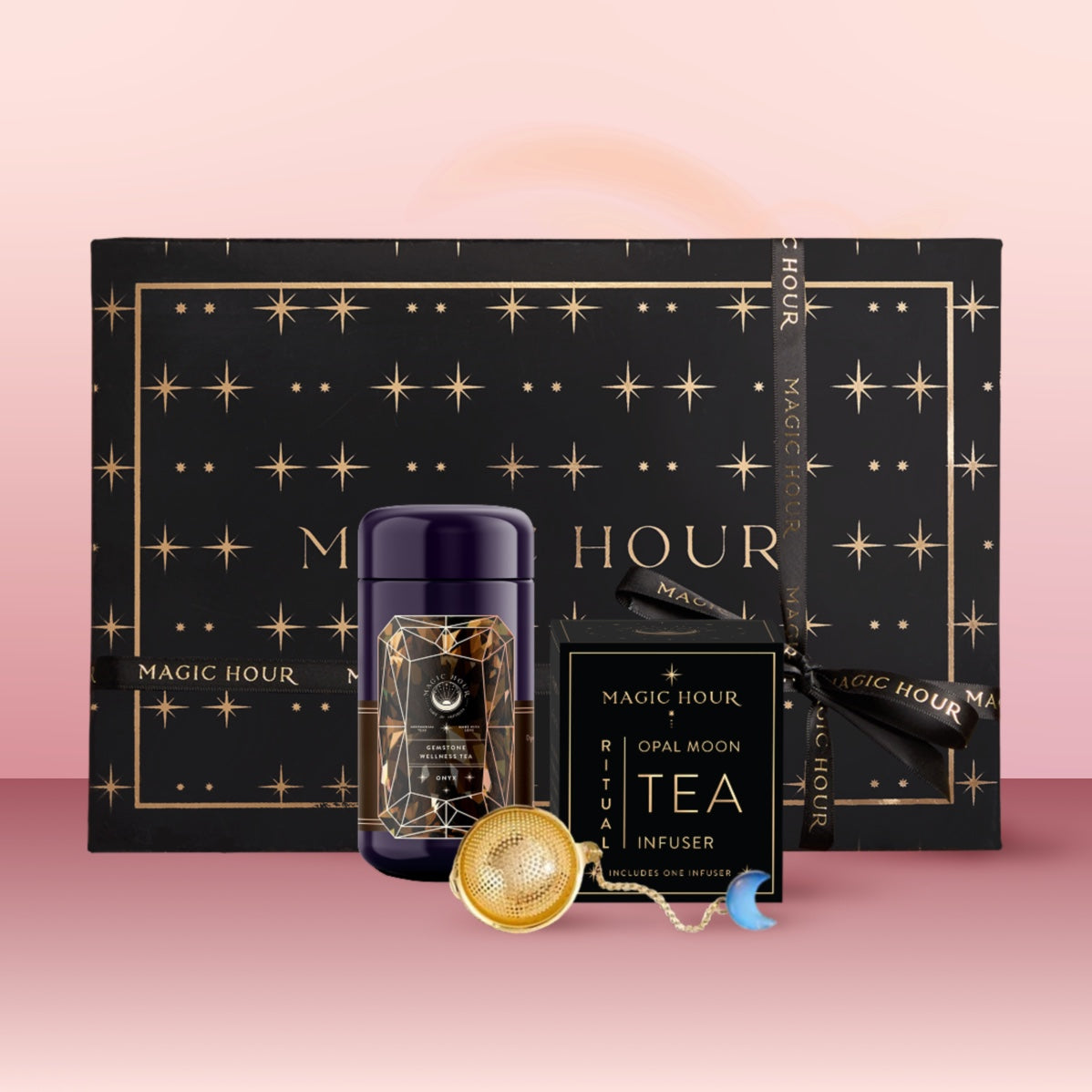 The Black Onyx December Birthstone Mini Gift Set features Black Onyx Wellness Tea in a star-patterned black box, a tea infuser, and an Opal Moon Tea Infuser box—an elegant wellness gift displayed on pink.