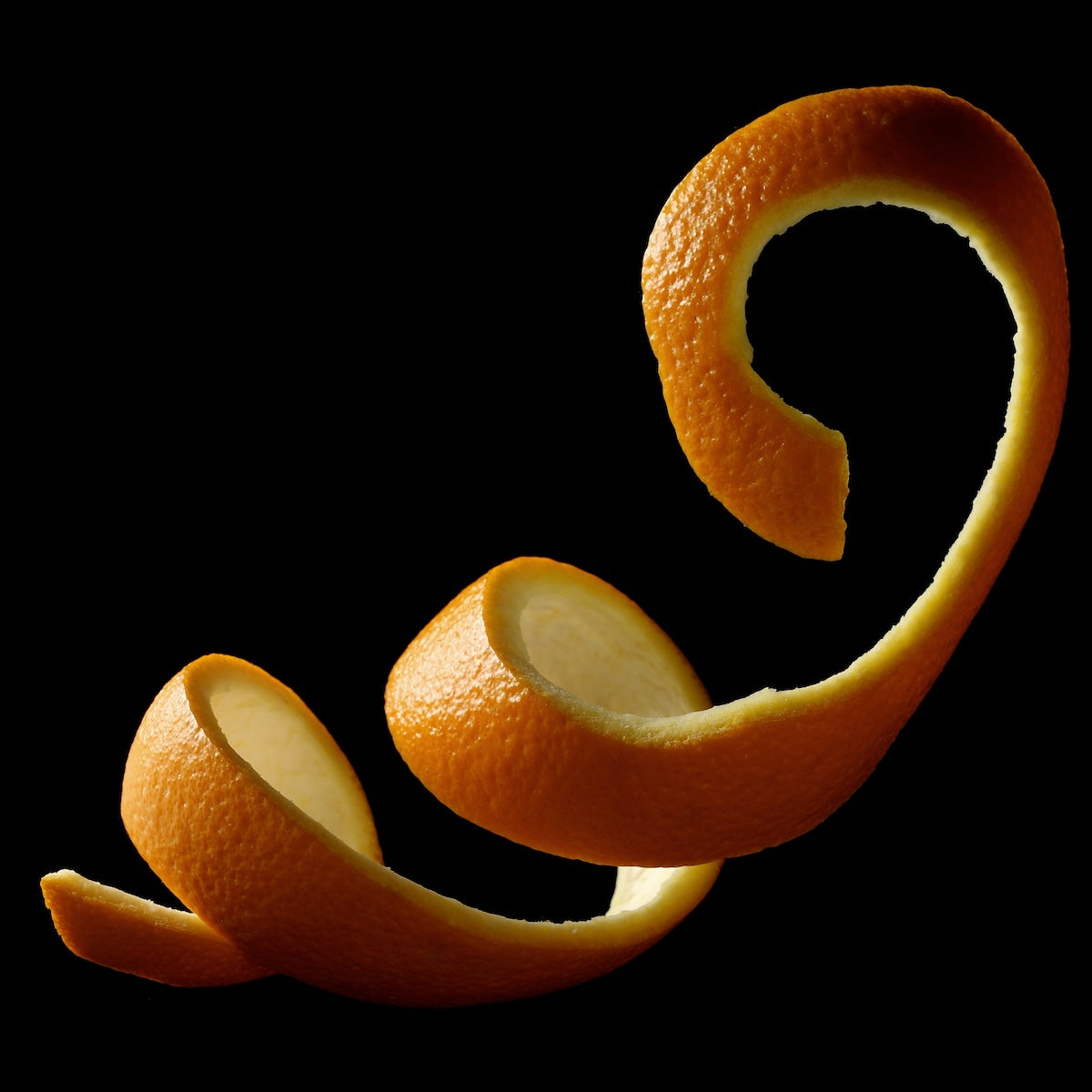 A spiraled orange peel against a black background. The peel curls gracefully with varying thickness, showcasing a textured orange surface on the outside and a smooth, light interior.