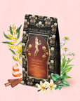 A Monthly Magic Tea Journey Subscription package is surrounded by herbs, cinnamon sticks, chamomile flowers, and vanilla on a pale pink background, evoking the sacred traditions of goddess archetypes and inviting you to create your own ritual guide.