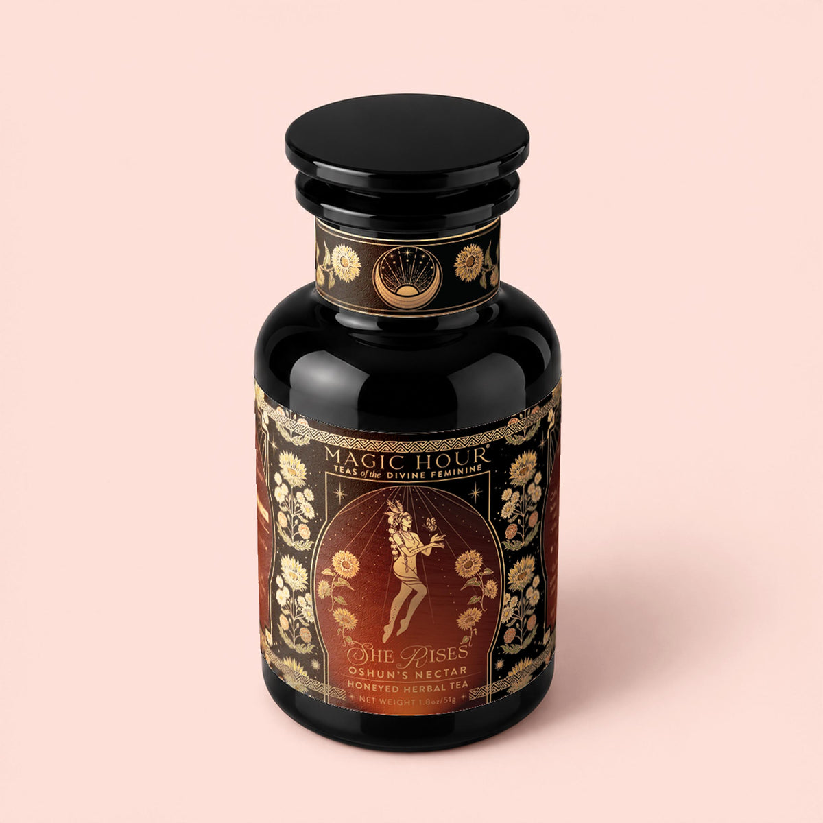 A dark glass jar labeled “Magic Hour: Oshun’s Nectar: Honeyed Herbal Tea for Joy &amp; Radiance,” adorned with ornate gold floral designs and an illustration of a woman holding a flute. This golden honeyed herbal tea combines soothing rooibos honeybush tea with delicate botanicals, offering a truly enchanting experience.