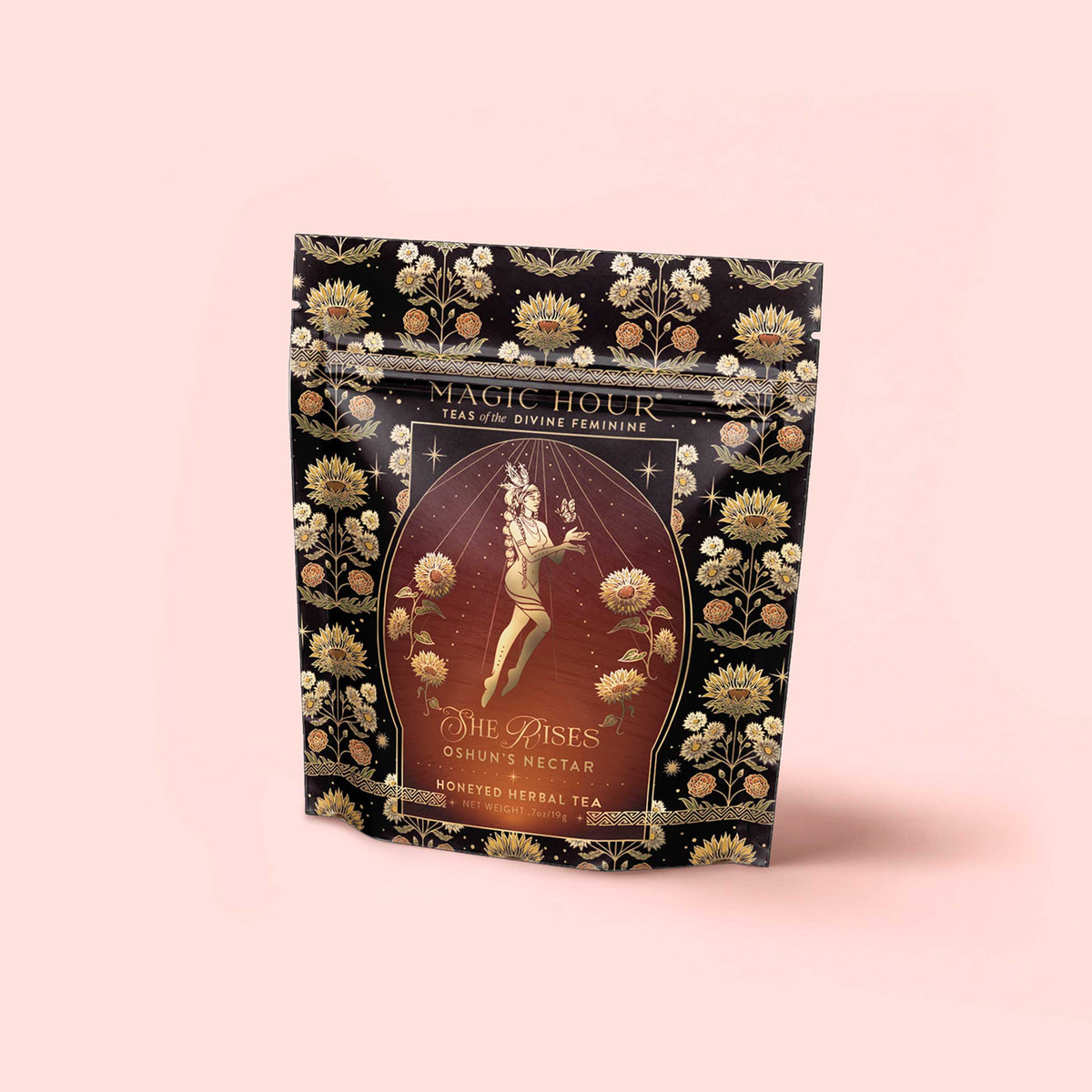 A floral-patterned bag from the Monthly Magic Tea Journey Subscription, featuring “She Rises: Oshun’s Nectar” honeyed herbal tea inspired by goddess archetypes, with an illustration of a woman adorned with flowers and gold accents on a peach background.