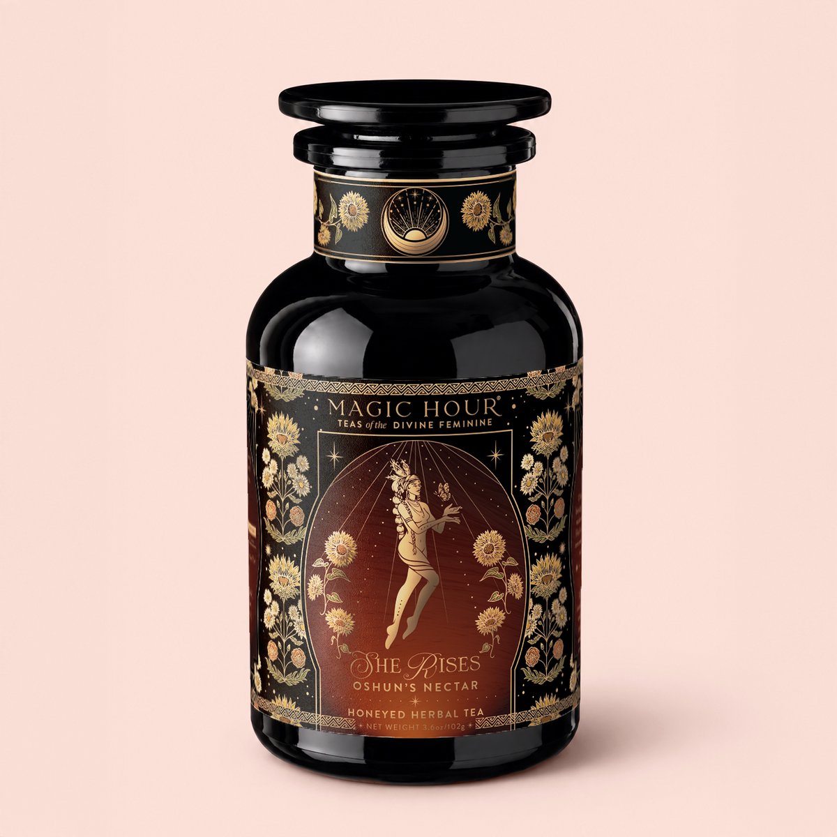 A dark, ornate tea jar labeled “Magic Hour: Teas of the Divine Feminine” features a floating female figure, gold floral designs, and text that reads “Oshun’s Nectar: Honeyed Herbal Tea for Joy &amp; Radiance.”.