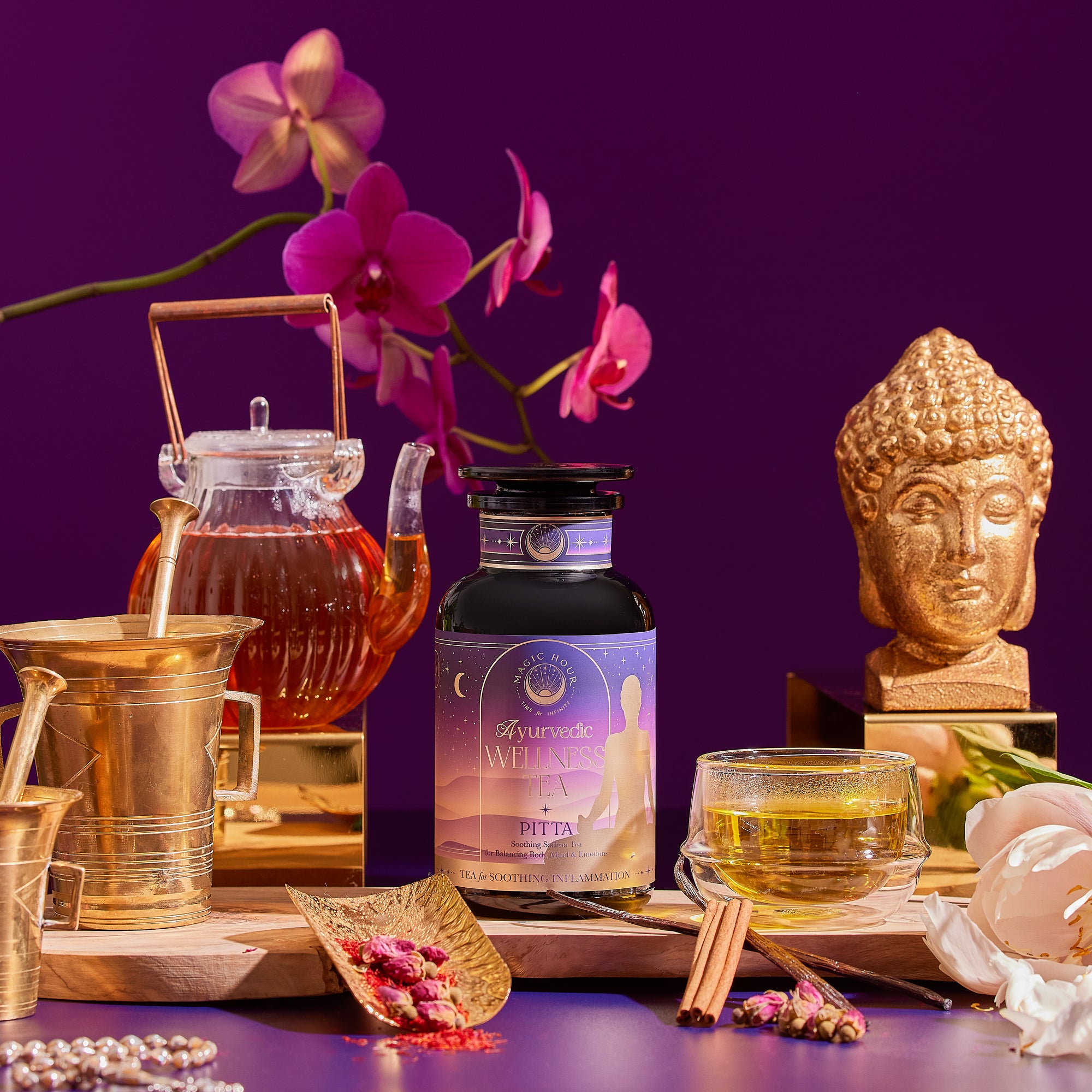A bottle labeled "Pitta Herbal" is displayed with a teapot, teacup, honey jar, cinnamon sticks, flowers, a golden Buddha head statue, and brass utensils against a purple background.
