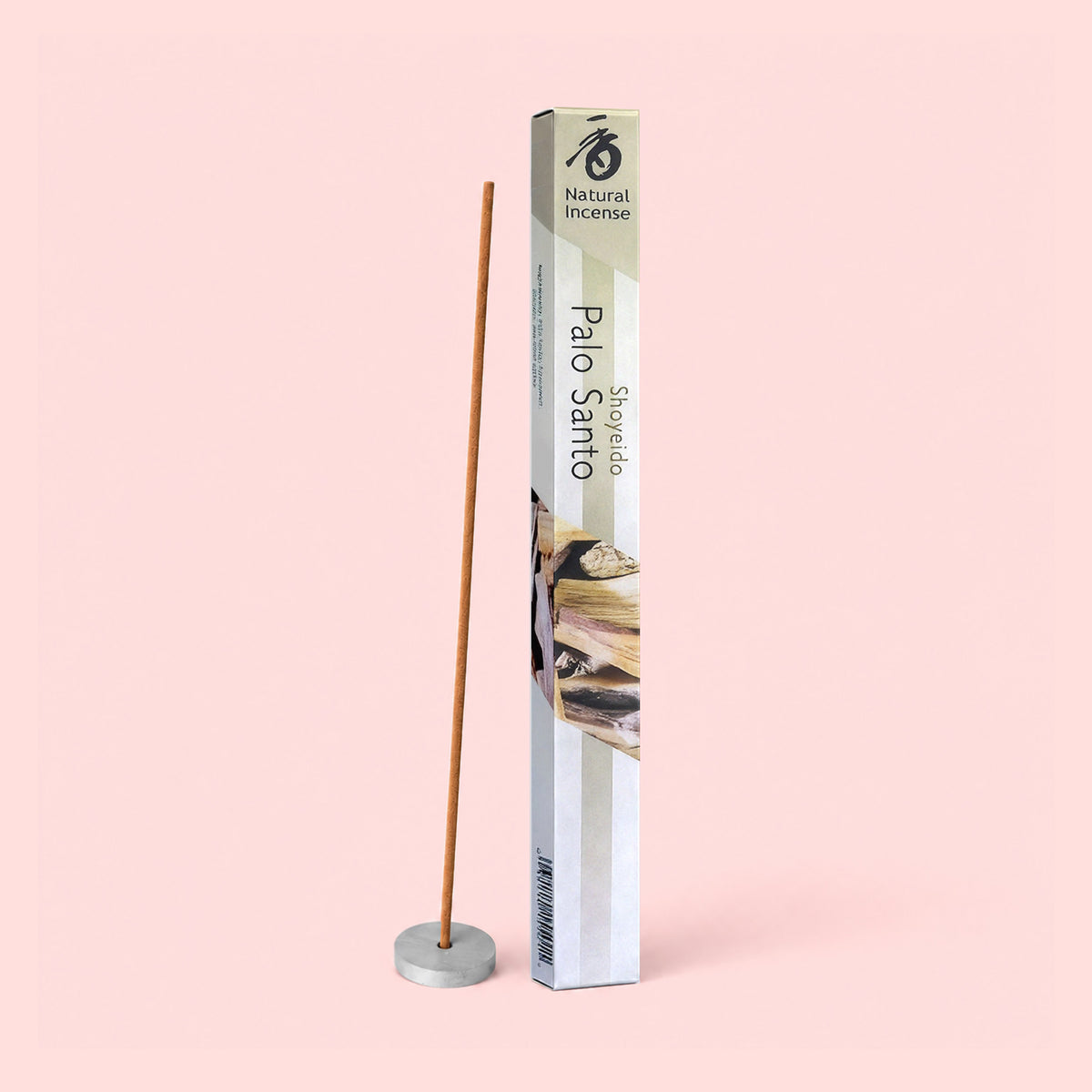 A Natural Incense : Palo Santo stick stands upright in a small holder beside its rectangular packaging, set against a pale pink background.