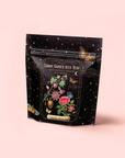The "Passionfruit Green with Roses Iced Tea" package displays vibrant flowers, fruit, a butterfly, gold stars, and celestial motifs on a light pink background for an uplifting mood.
