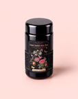 A black tea canister labeled “Passionfruit Green with Roses Iced Tea,” featuring colorful floral and fruit illustrations, set against a light pink background—perfect for enjoying a refreshing, metabolism boosting passionfruit green tea.