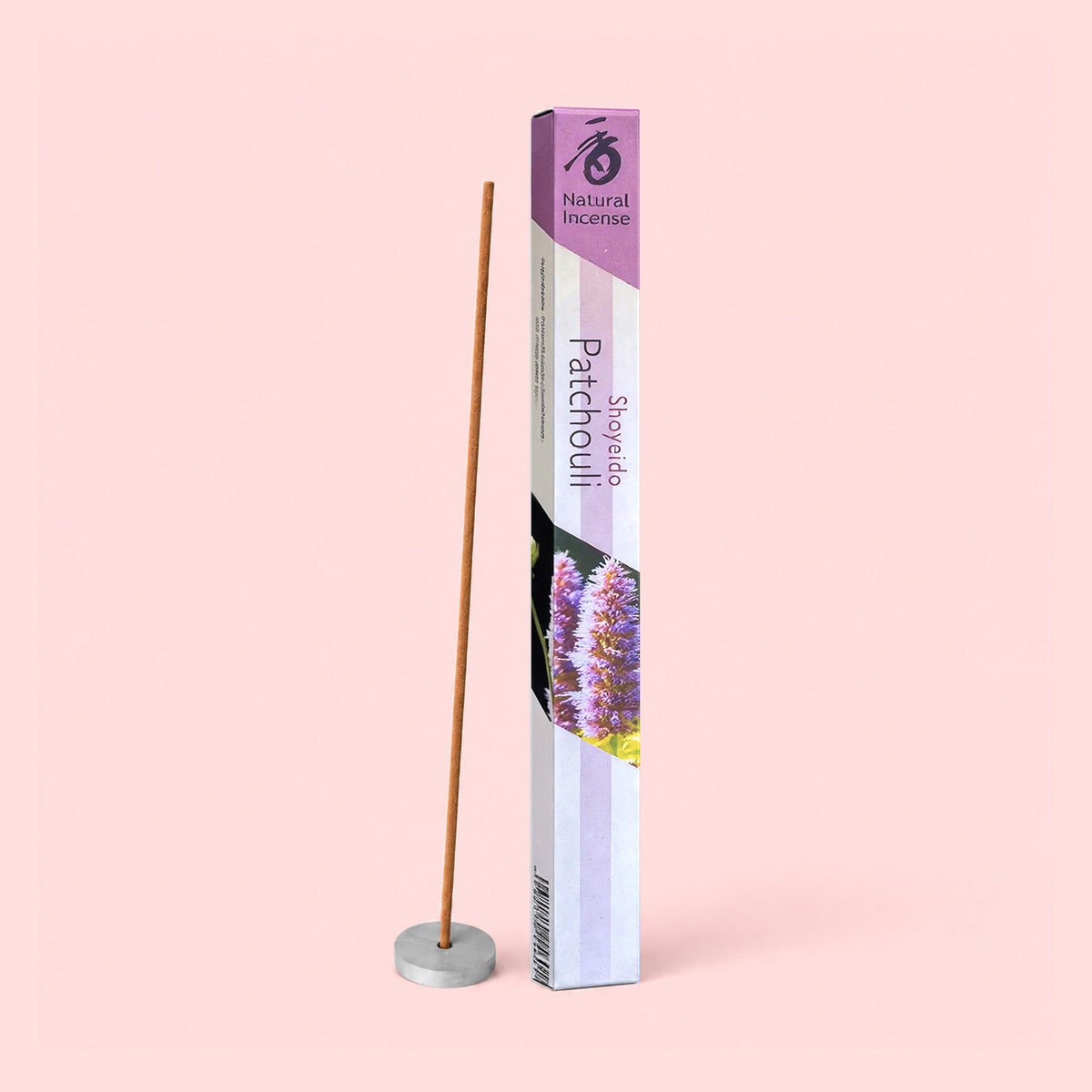 A box of Natural Incense : Patchouli stands upright next to a single incense stick held in a small round holder, set against a light pink background.