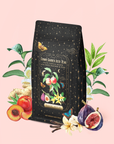 A package of Peach Vanilla Black Iced Tea with Figs features gold stars, fruit illustrations (peach and fig), and floral designs, all surrounded by fresh fruit and leaves on a pink background. The label reads "Cosmic Garden Iced Teas" from Magic Hour. Enjoy this calorie-free tea experience that blends the lush sweetness of peaches and vanilla with figs, capturing the vibrant essence of a summertime garden.