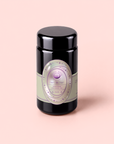 A black tea canister labeled “Pearl Tea of Beauty, Clarity, and a Sense of Peace,” adorned with pastel green and lavender accents and featuring soothing Tulsi and organic chamomile, sits on a light pink background.