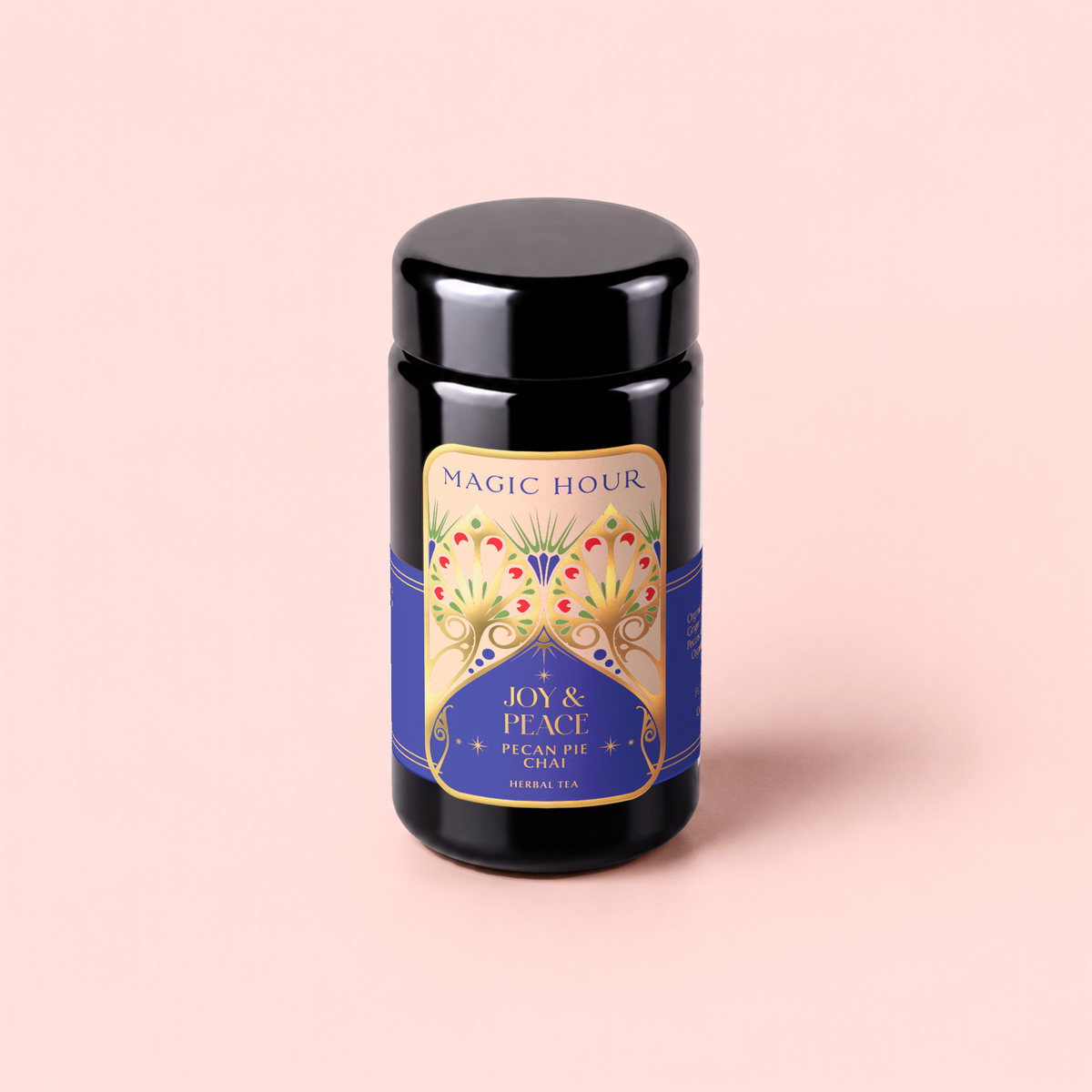A black tea canister labeled “Magic Hour Pecan Pie Chai,” featuring an ornate gold and blue design, sits against a pale pink background. This soothing blend combines calming ashwagandha with aromatic chai spices for a restorative experience.