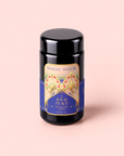 A black tea canister labeled “Magic Hour Pecan Pie Chai,” featuring an ornate gold and blue design, sits against a pale pink background. This soothing blend combines calming ashwagandha with aromatic chai spices for a restorative experience.